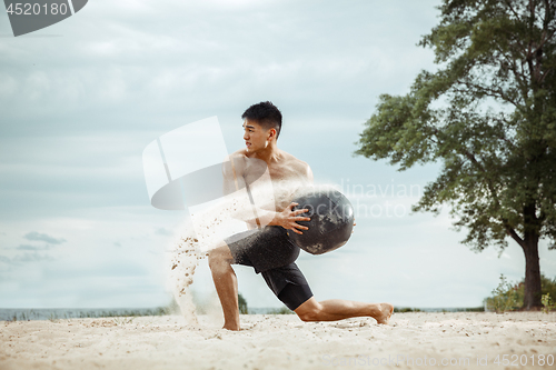 Image of Young healthy man athlete doing squats at the beach