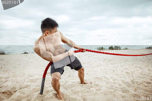 Image of Young healthy man athlete doing squats at the beach