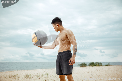 Image of Young healthy man athlete doing squats at the beach