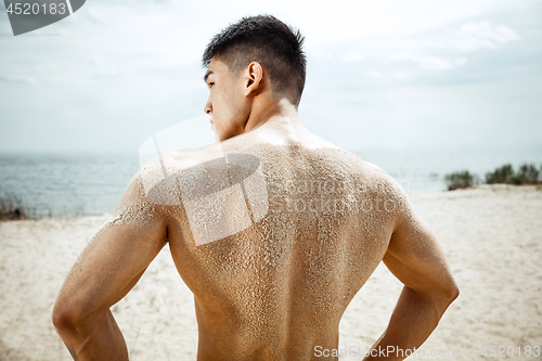 Image of Young healthy man athlete doing squats at the beach