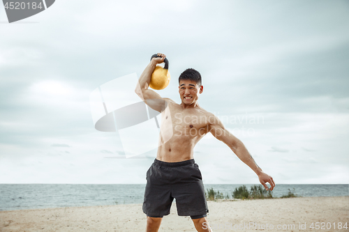 Image of Young healthy man athlete doing squats at the beach