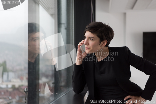 Image of Elegant Woman Using Mobile Phone by window in office building