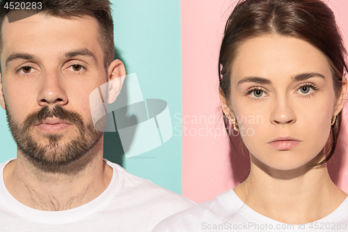 Image of The serious man and woman looking at camera against pink and blue background.