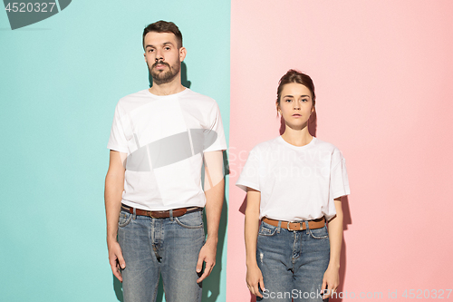 Image of The serious man and woman looking at camera against pink and blue background.