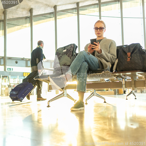 Image of Female traveler using her cell phone while waiting to board a plane at departure gates at airport terminal.