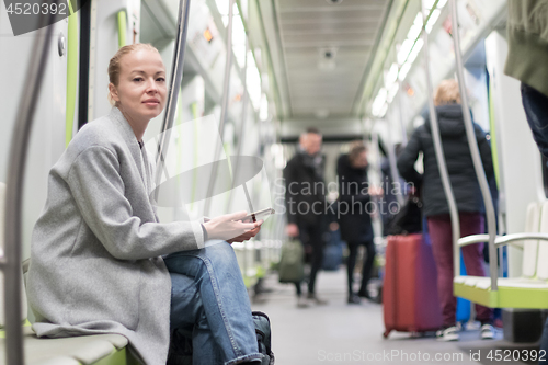 Image of Beautiful blonde woman using smart phone while traveling by metro public transport.