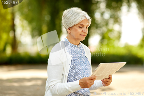 Image of senior woman reading newspaper at summer park