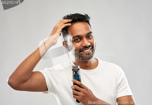 Image of smiling indian man with trimmer touching his hair