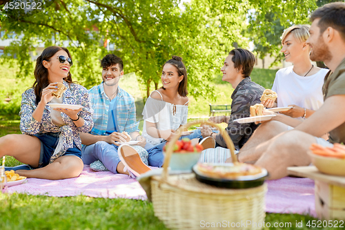 Image of happy friends eating sandwiches at summer picnic