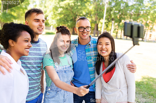 Image of happy friends taking photo by selfie stick at park