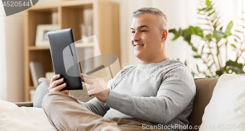 Image of man with tablet pc and credit card on sofa at home