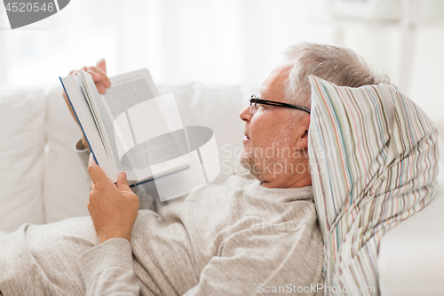 Image of senior man lying on sofa and reading book at home