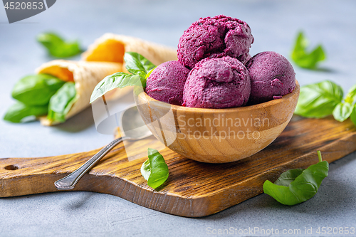 Image of Blueberry ice cream balls and green basil in a wooden bowl.