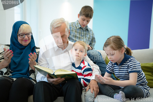 Image of modern muslim grandparents with grandchildren reading Quran