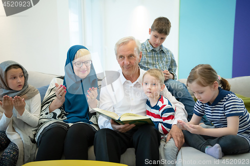 Image of modern muslim grandparents with grandchildren reading Quran