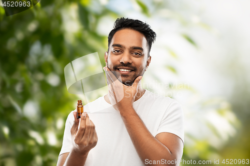 Image of indian man applying natural grooming oil to beard