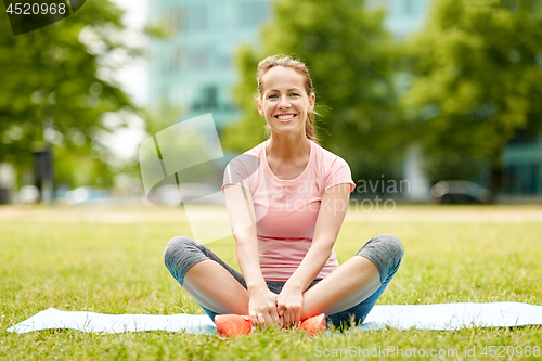 Image of woman sitting on exercise mat at park in summer