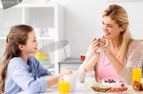 Image of happy mother and daughter having breakfast at home