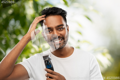 Image of smiling indian man with trimmer touching his hair