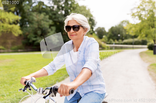 Image of happy senior woman riding bicycle at summer park