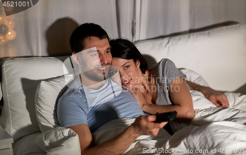 Image of happy couple watching tv in bed at night at home