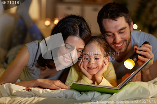 Image of happy family reading book in bed at night at home