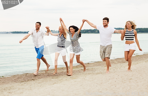 Image of friends in striped clothes running along beach