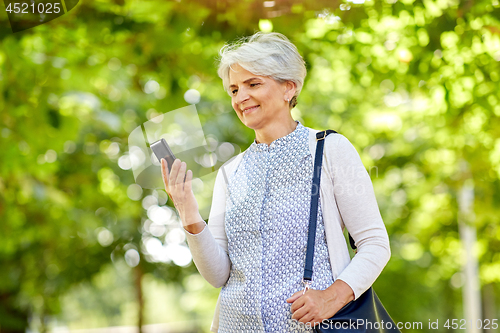 Image of happy senior woman with smartphone at summer park