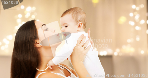 Image of mother kissing baby over christmas lights