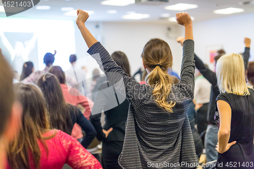 Image of Participants of interactive motivational speech feeling empowered and motivated, hands raised high in the air.