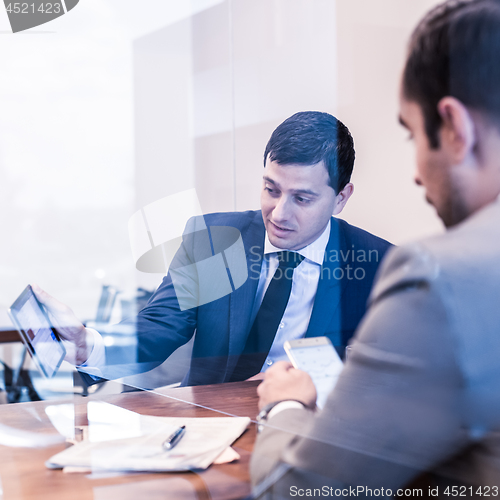 Image of Two young businessmen using electronic devices at business meeting.