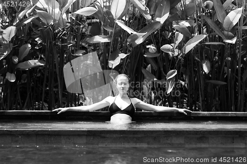 Image of Sensual young woman relaxing in outdoor spa infinity swimming pool surrounded with lush tropical greenery of Ubud, Bali. Black and white image.