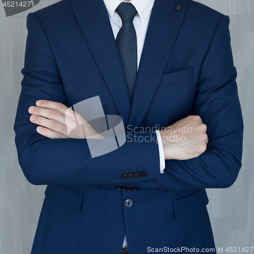 Image of Torso of anonymous businessman standing with hands in lowered steeple wearing beautiful fashionable classic grey suit, white shirt and blue tie.