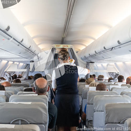 Image of Interior of commercial airplane with stewardess serving passengers on seats during flight.