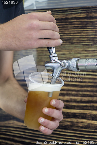 Image of Barmen filling plastic glass with light beer