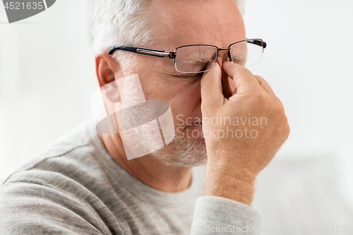 Image of senior man in glasses massaging nose bridge