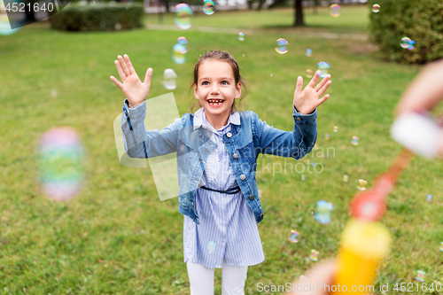 Image of happy girl playing with soap bubbles at park