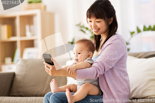 Image of asian mother with baby son taking selfie at home