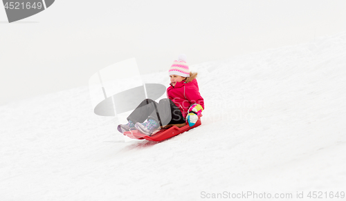 Image of happy little girl sliding down on sled in winter