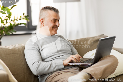 Image of man with laptop computer sitting on sofa at home
