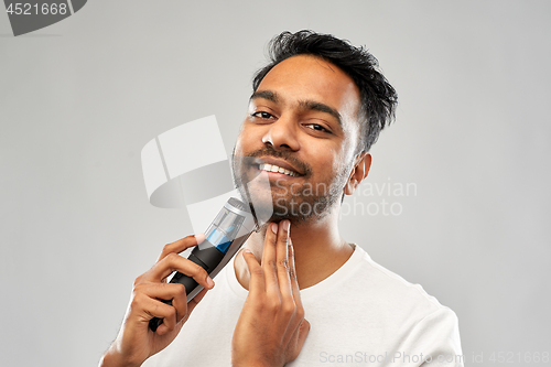 Image of smiling indian man shaving beard with trimmer