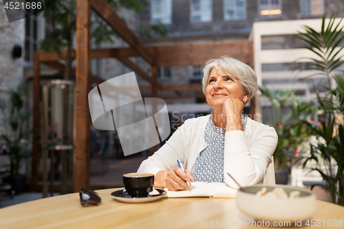 Image of senior woman with notebook dreaming at street cafe