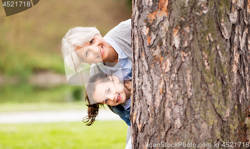 Image of grandmother and granddaughter behind tree at park