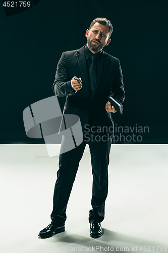 Image of Male beauty concept. Portrait of a fashionable young man with stylish haircut wearing trendy suit posing over black background.