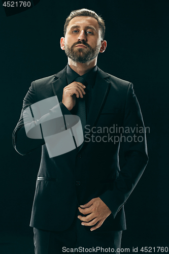 Image of Male beauty concept. Portrait of a fashionable young man with stylish haircut wearing trendy suit posing over black background.