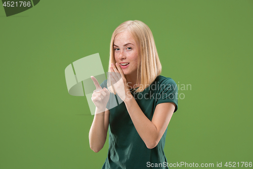 Image of The young woman whispering a secret behind her hand over green background