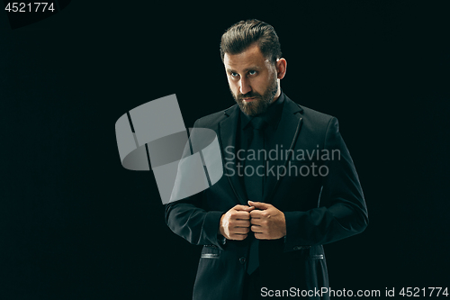 Image of Male beauty concept. Portrait of a fashionable young man with stylish haircut wearing trendy suit posing over black background.