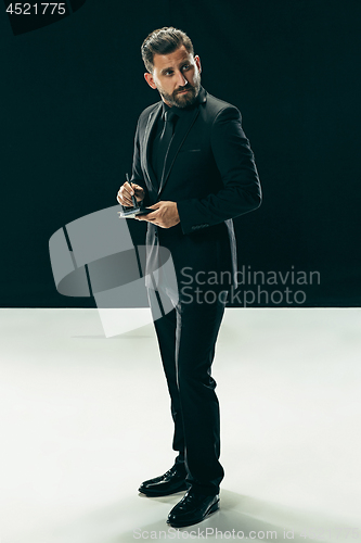 Image of Male beauty concept. Portrait of a fashionable young man with stylish haircut wearing trendy suit posing over black background.