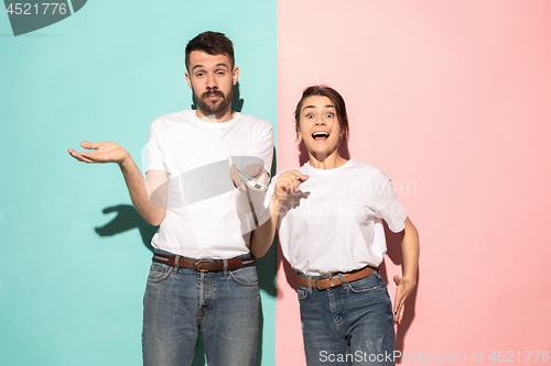 Image of Closeup portrait of young couple, man, woman. One being excited happy smiling, other serious, concerned, unhappy on pink and blue background. Emotion contrasts