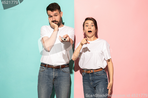 Image of Closeup portrait of young couple, man, woman. One being excited happy smiling, other serious, concerned, unhappy on pink and blue background. Emotion contrasts